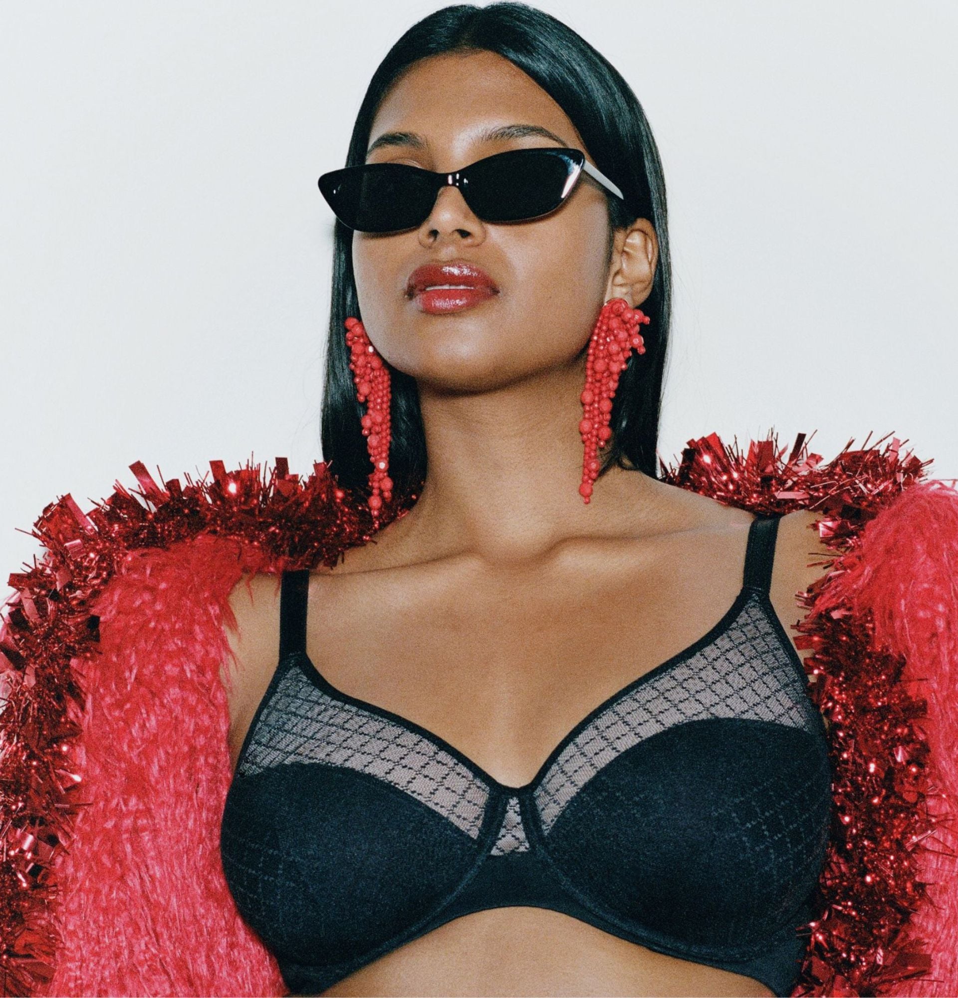 A woman is shown wearing a black lace bra, bold red earrings, sleek sunglasses, and a red textured shawl, creating a glamorous and festive look.