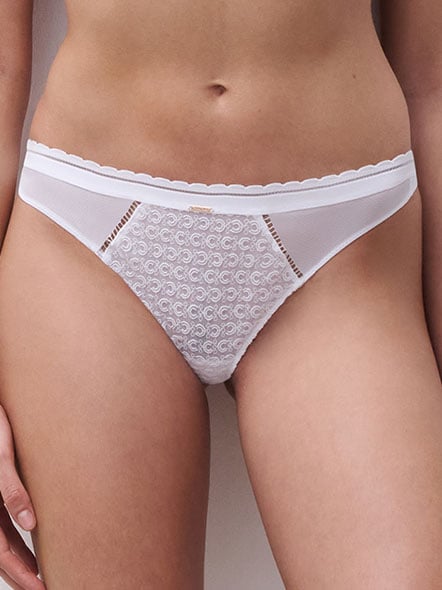 A person wearing white lace and mesh panties with a scalloped edge and decorative gold detail.