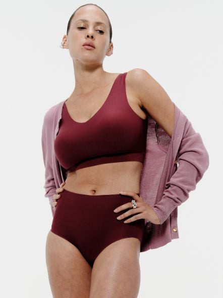 Person posing confidently in burgundy underwear and a matching cardigan against a plain white background.