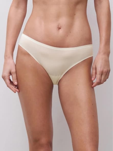 A person wearing cream-colored bikini underwear, standing against a plain background. The focus is on the lower torso.