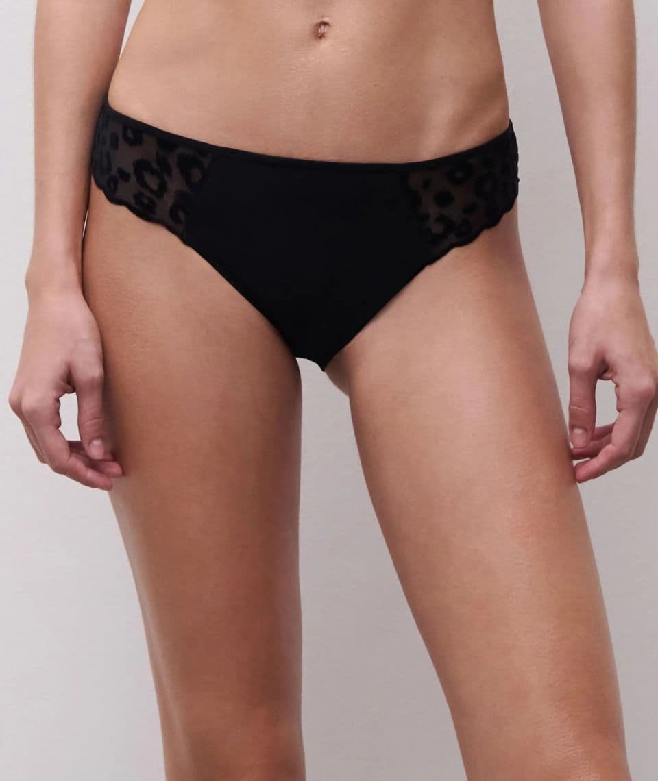 Person wearing black bottoms with leopard print mesh panels on the sides, standing against a plain background.