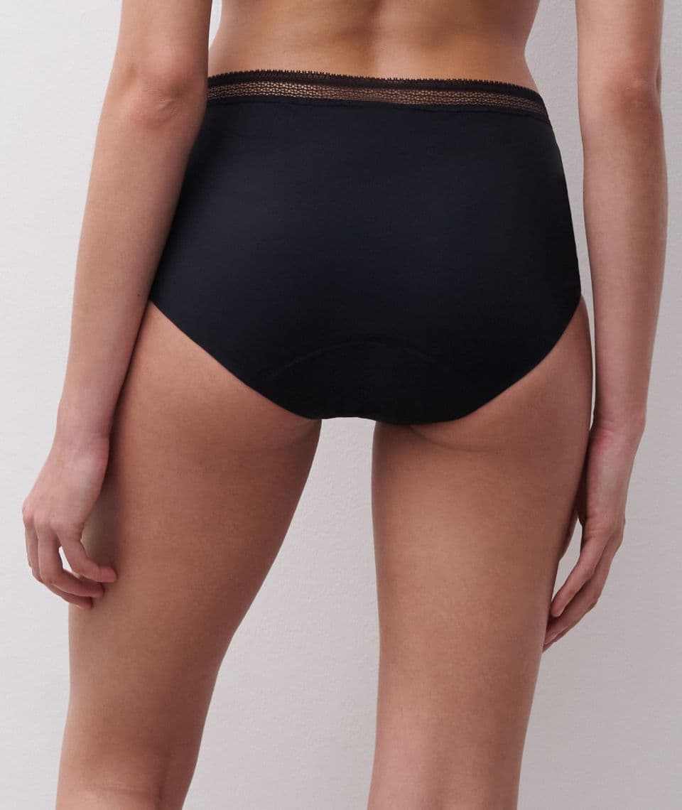 Rear view of a person wearing black high-waisted underwear with lace trim at the waistband, standing against a plain background.