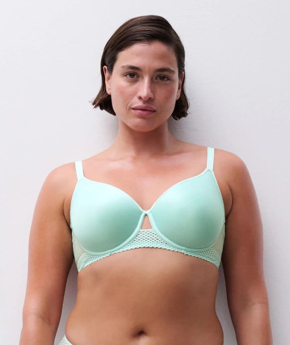 Person wearing a light green bra with a mesh detail, standing against a plain white background.