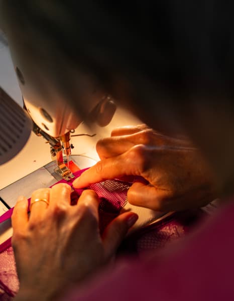 Une personne cousant du tissu en dentelle rose à l'aide d'une machine à coudre, en mettant l'accent sur la zone de l'aiguille et les détails du tissu.