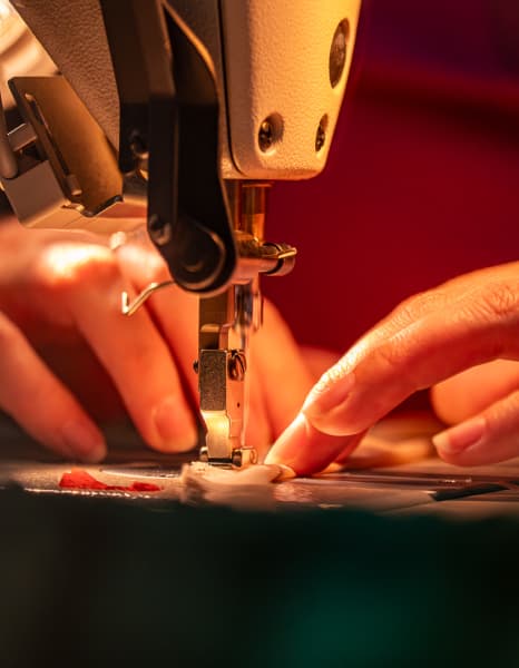 Des mains guidant le tissu à travers une machine à coudre, concentrées sur la couture sous un éclairage chaleureux et ciblé.